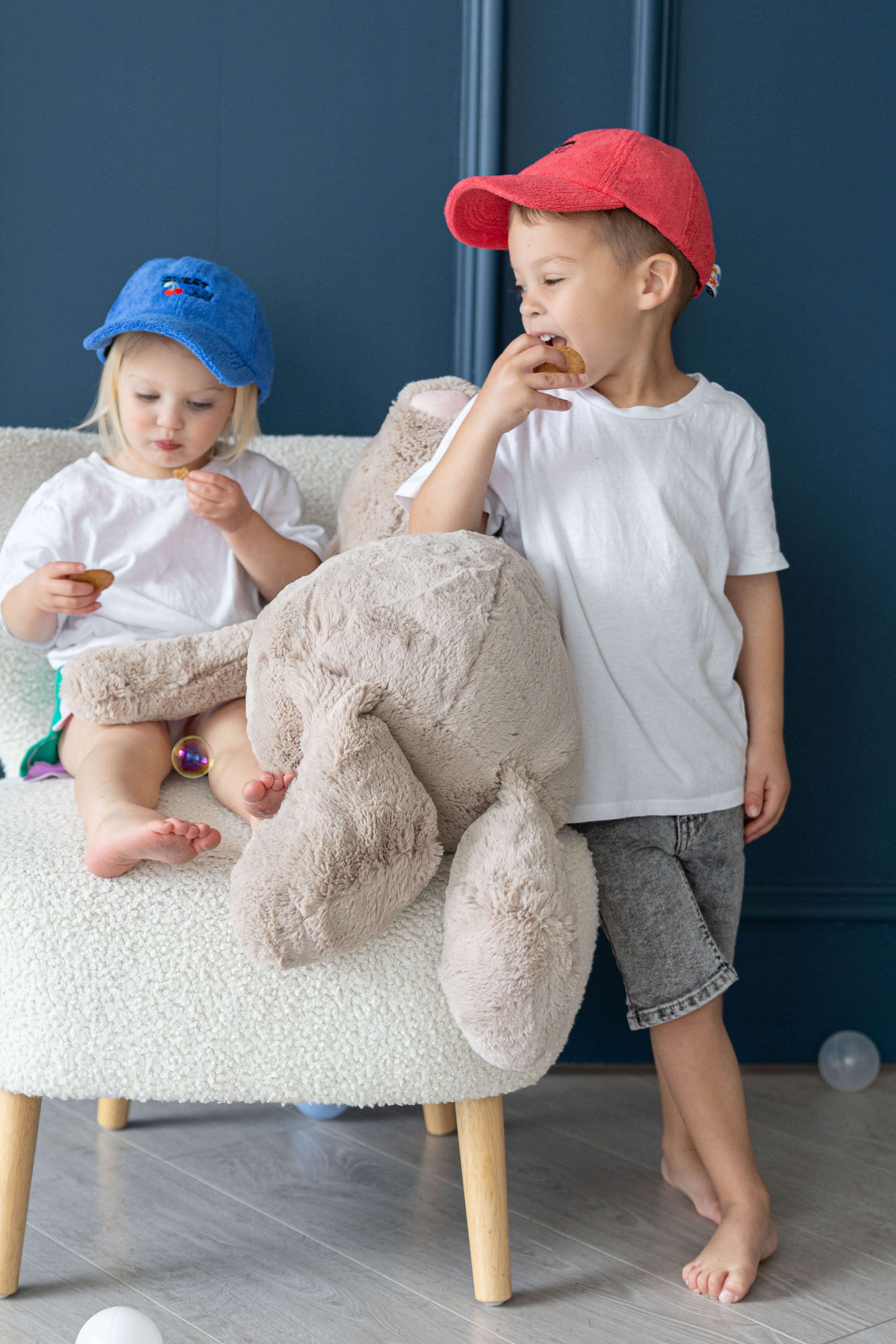 Two children playing with a plush toy on a chair against a blue wall.