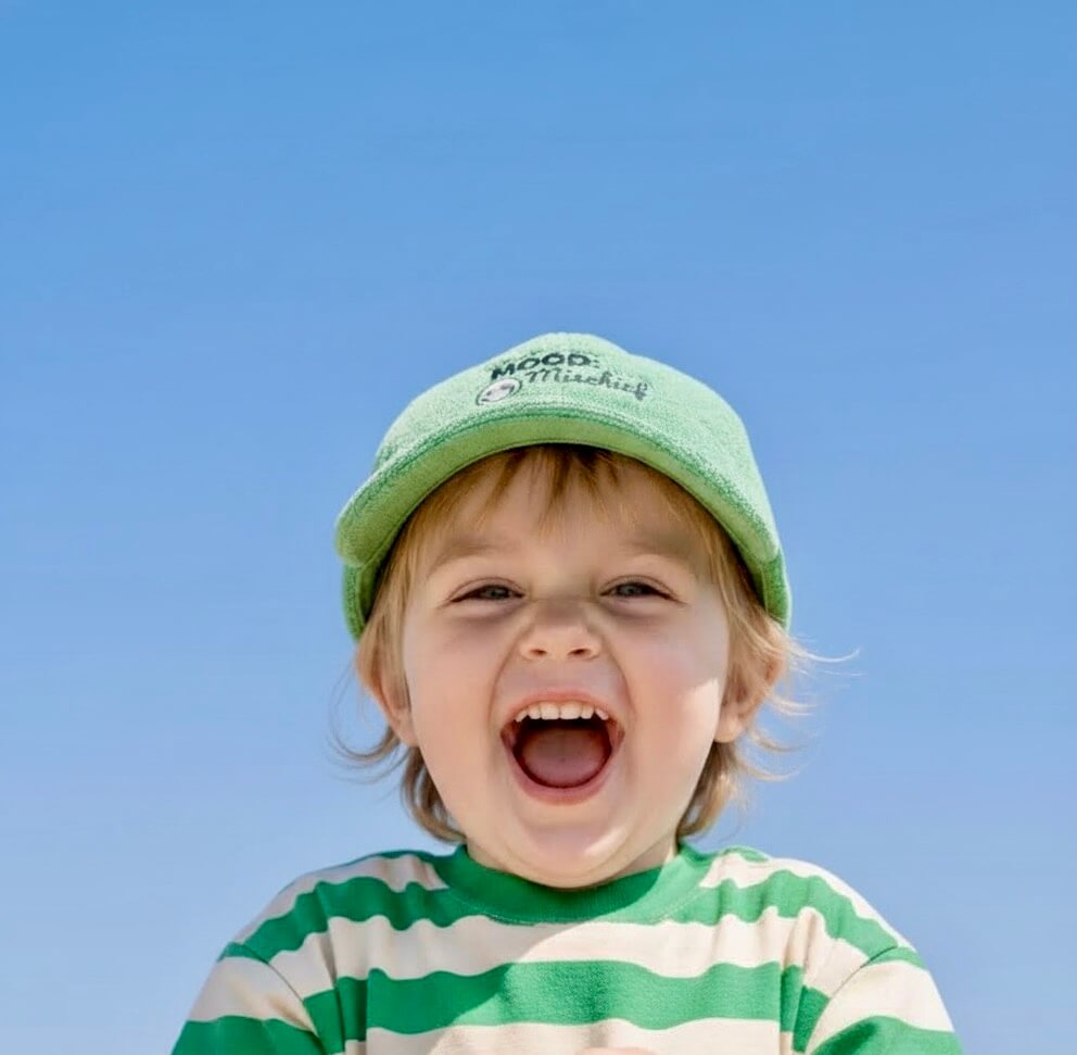 Child wearing a green cap and striped shirt against a clear blue sky