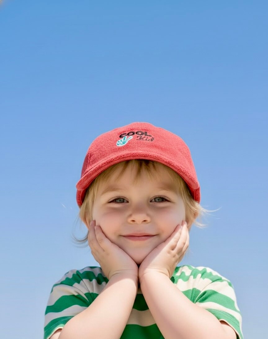 Child wearing a red cap and green striped shirt against a clear blue sky