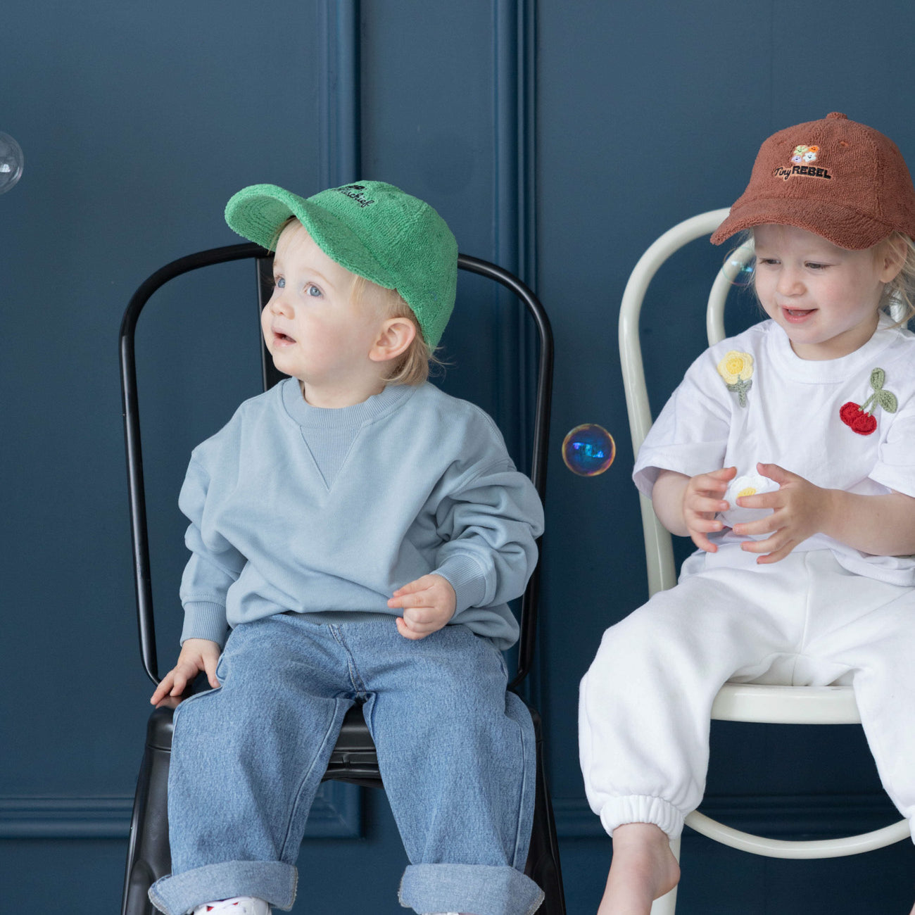 Two children sitting on chairs with a blue wall and bubbles in the background