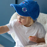 Child wearing a blue terry towelling hat with a 'sweet child' embroidery design, sitting on a couch.