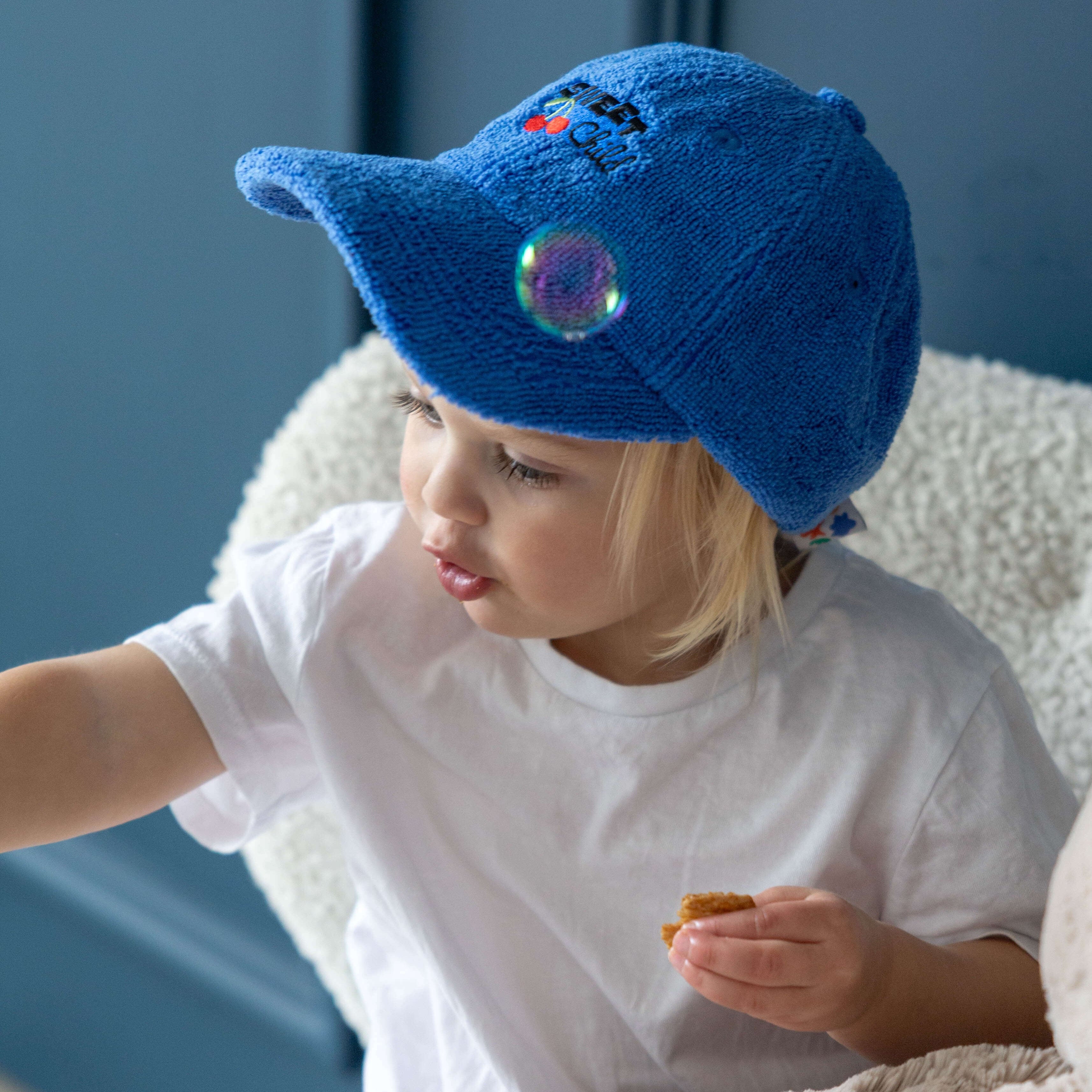 Child wearing a blue terry towelling hat with a 'sweet child' embroidery design, sitting on a couch.