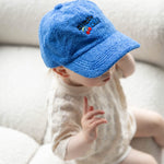Baby wearing a blue cap sitting on a white couch
