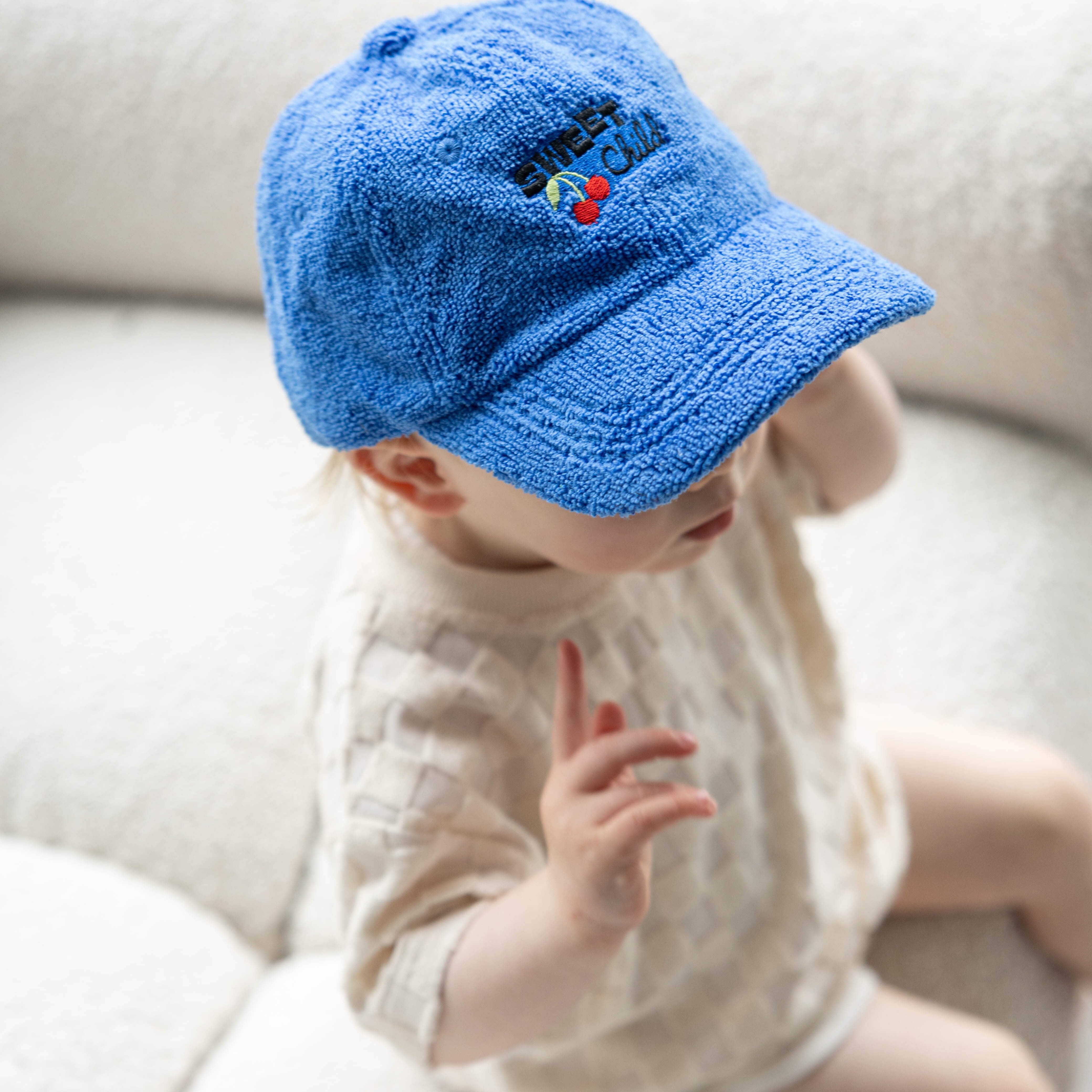 Baby wearing a blue cap sitting on a white couch
