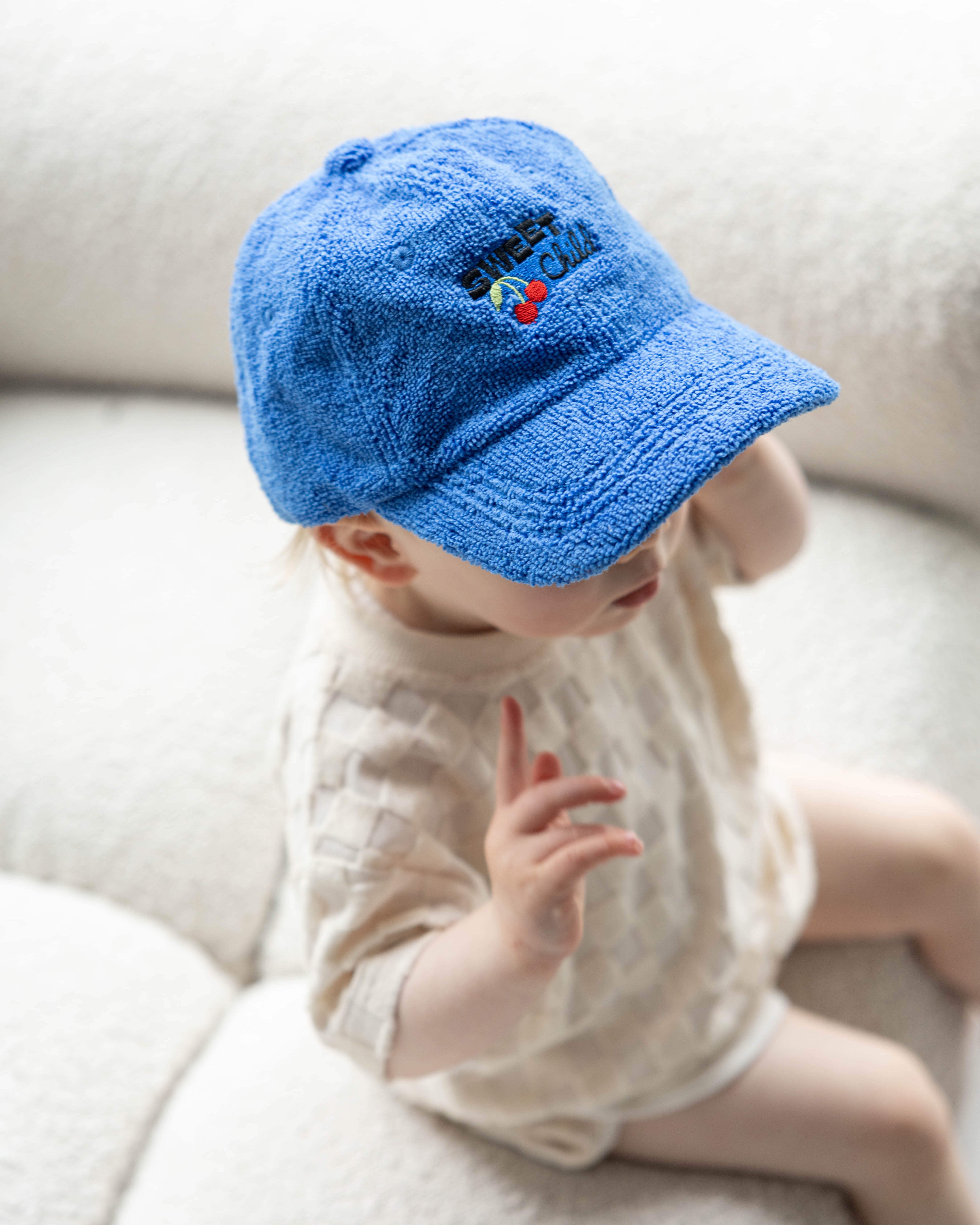 Baby wearing a blue cap sitting on a white couch