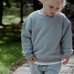 Child wearing a light blue sweater and pants outdoors