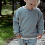 Child wearing a light blue sweater and pants outdoors