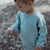 Child wearing a light blue sweater holding a flower on a textured ground.