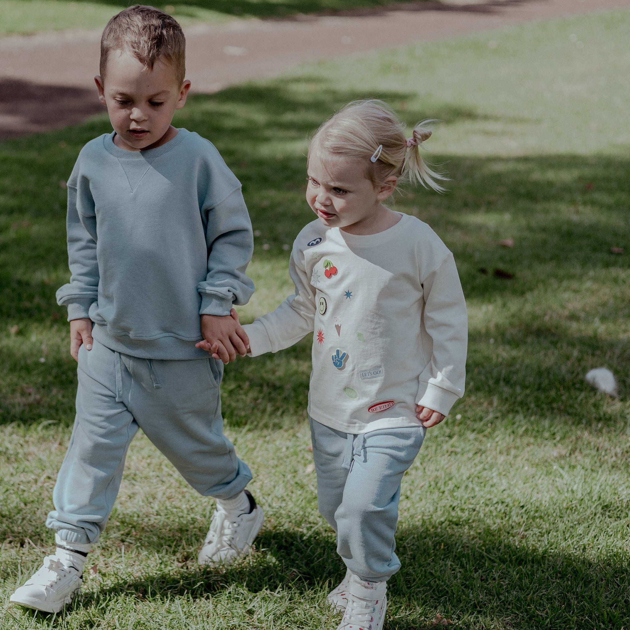 Two children in blue sweatpants holding hands on a grassy field