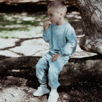 Child in light blue tracksuit sitting on a log in a natural setting