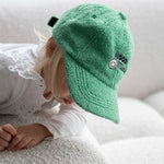 Child wearing a green cap with a smiley face logo on a white couch