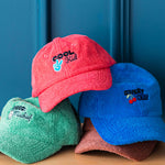 Four colorful caps with embroidered text on a wooden surface against a blue wall.