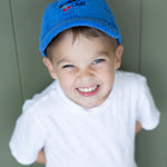 Child wearing a blue cap and white shirt against a green background