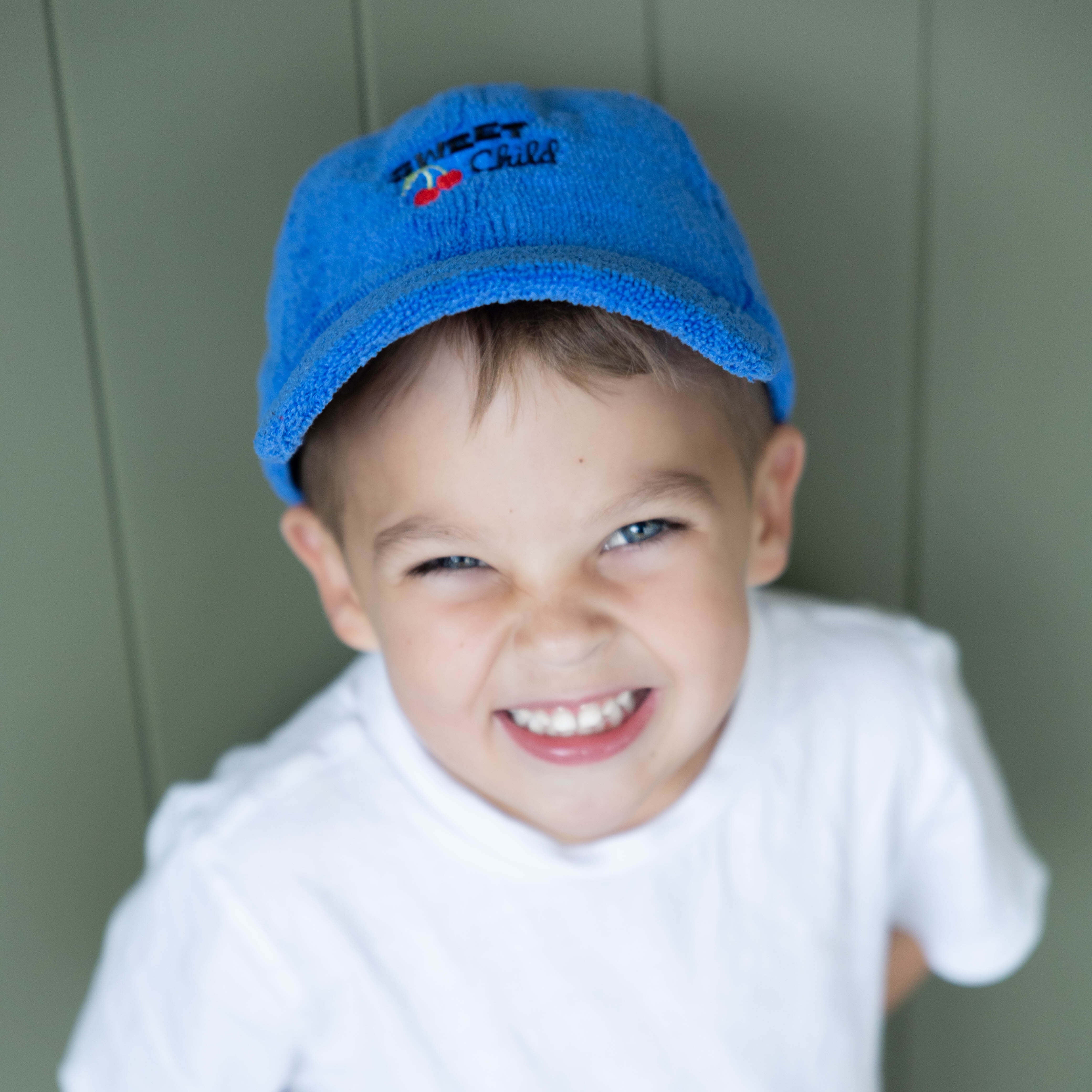 Child wearing a blue cap and white shirt against a green background