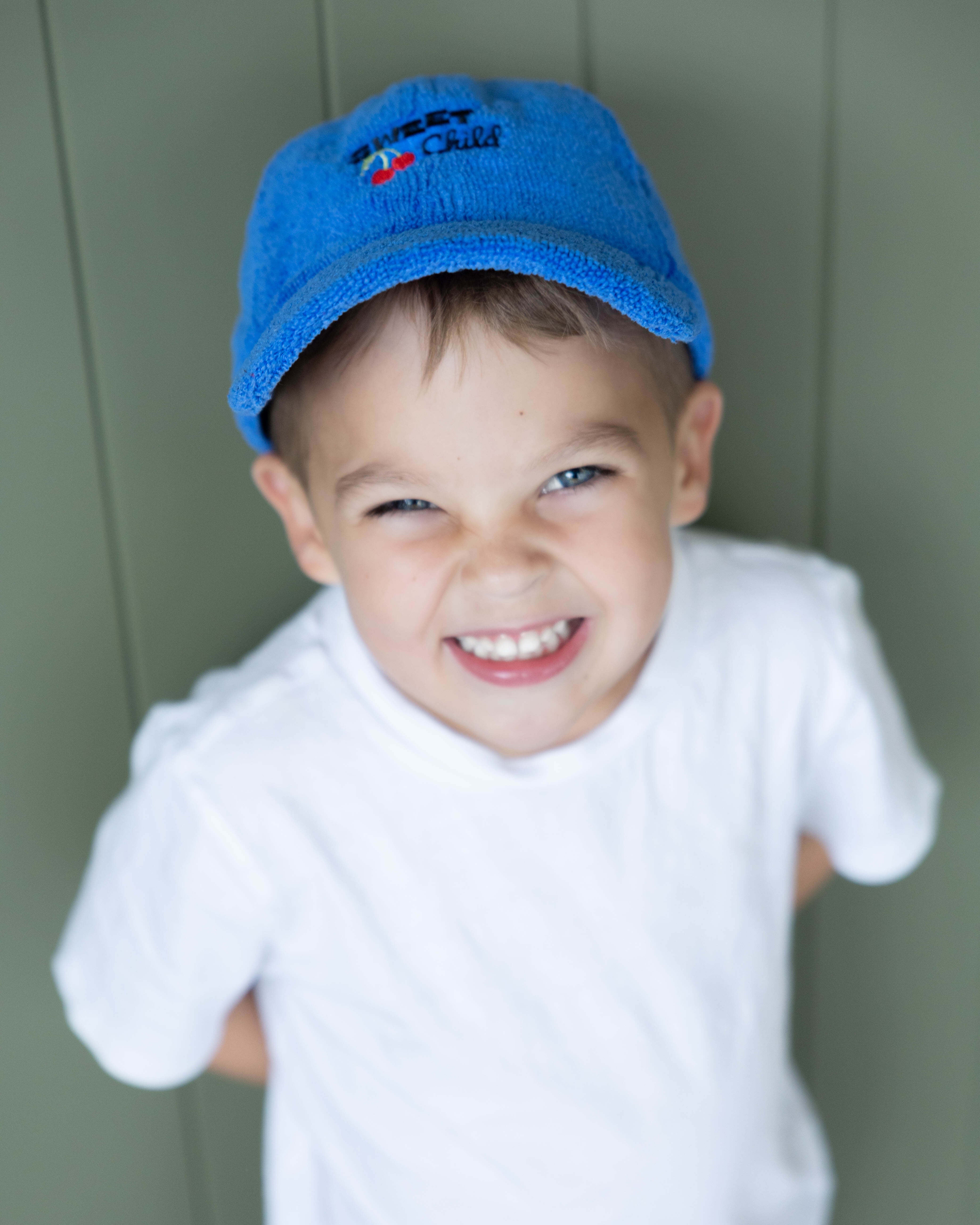 Child wearing a blue cap and white shirt against a green background
