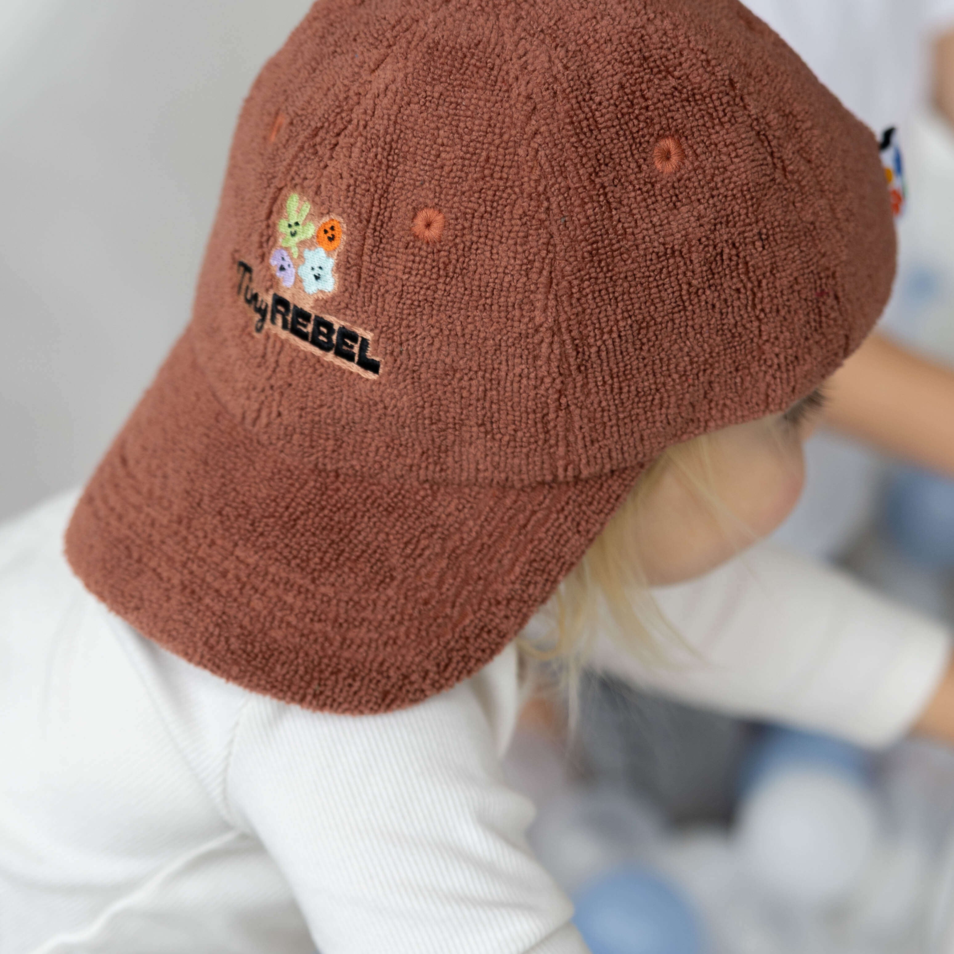 Child wearing a brown terry towelling cap with embroidery, standing in a playground.