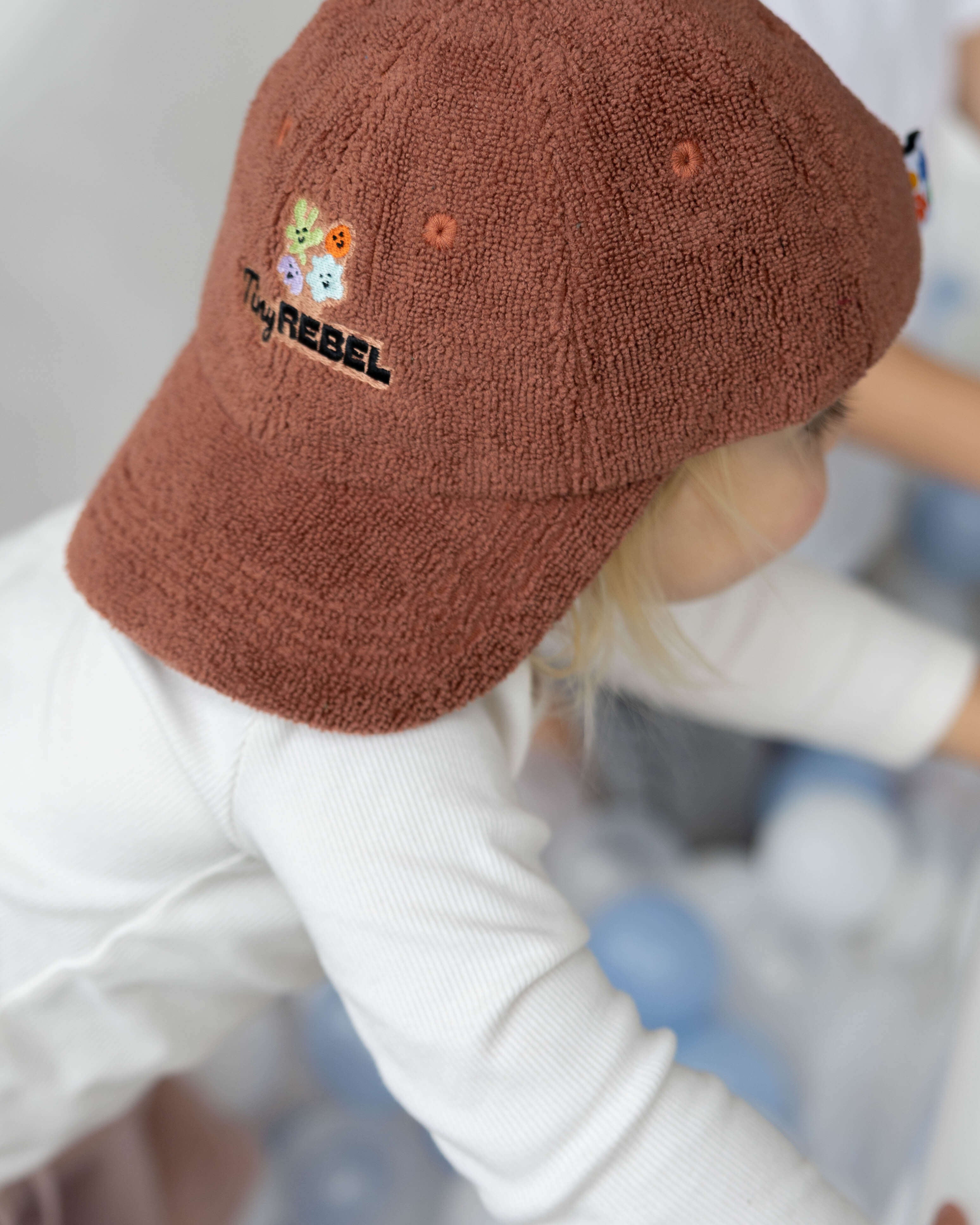 Child wearing a brown terry towelling cap with embroidery, standing in a playground.