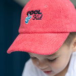 Child wearing a red cap with 'Cool Kid' text and peace sign.