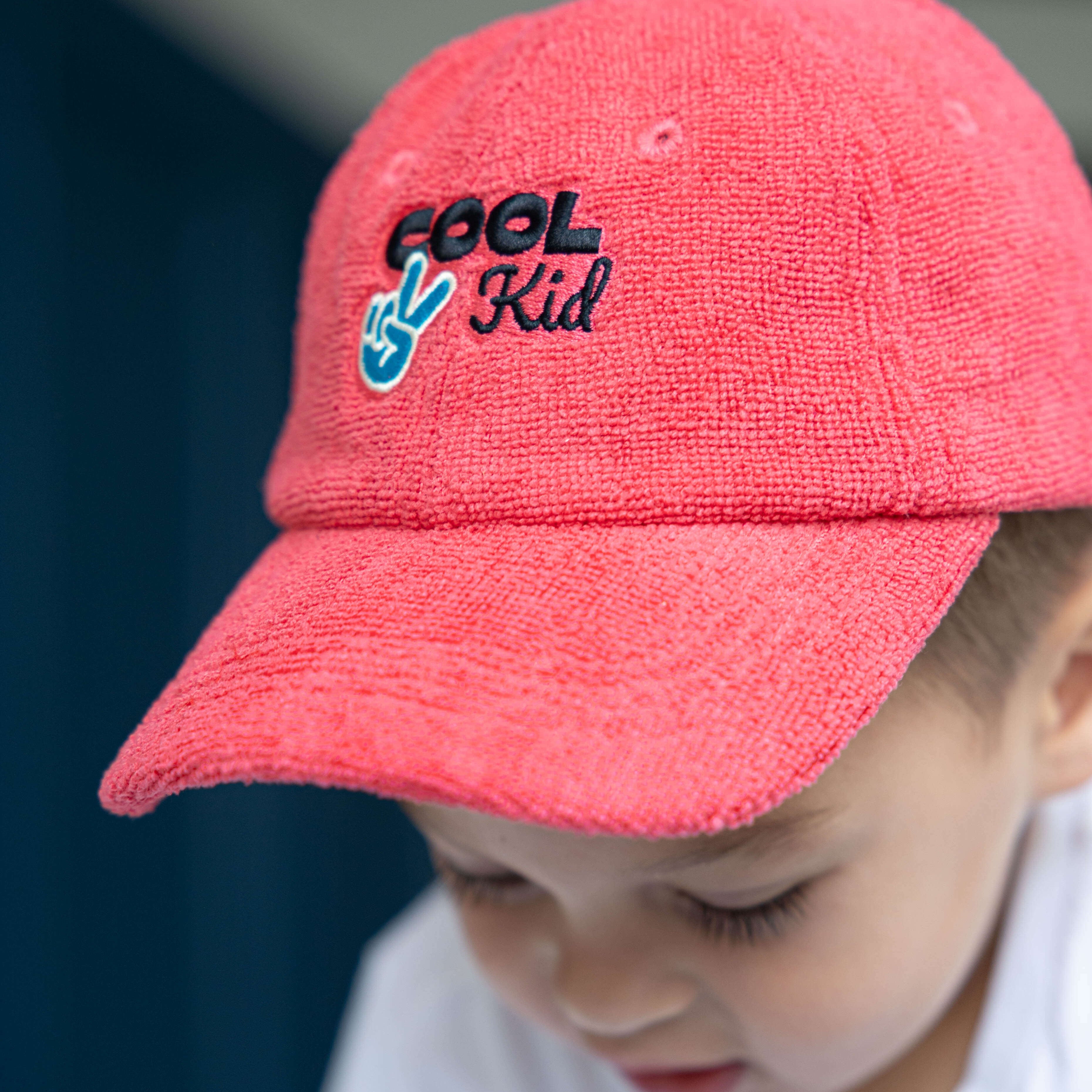 Child wearing a red cap with 'Cool Kid' text and peace sign.