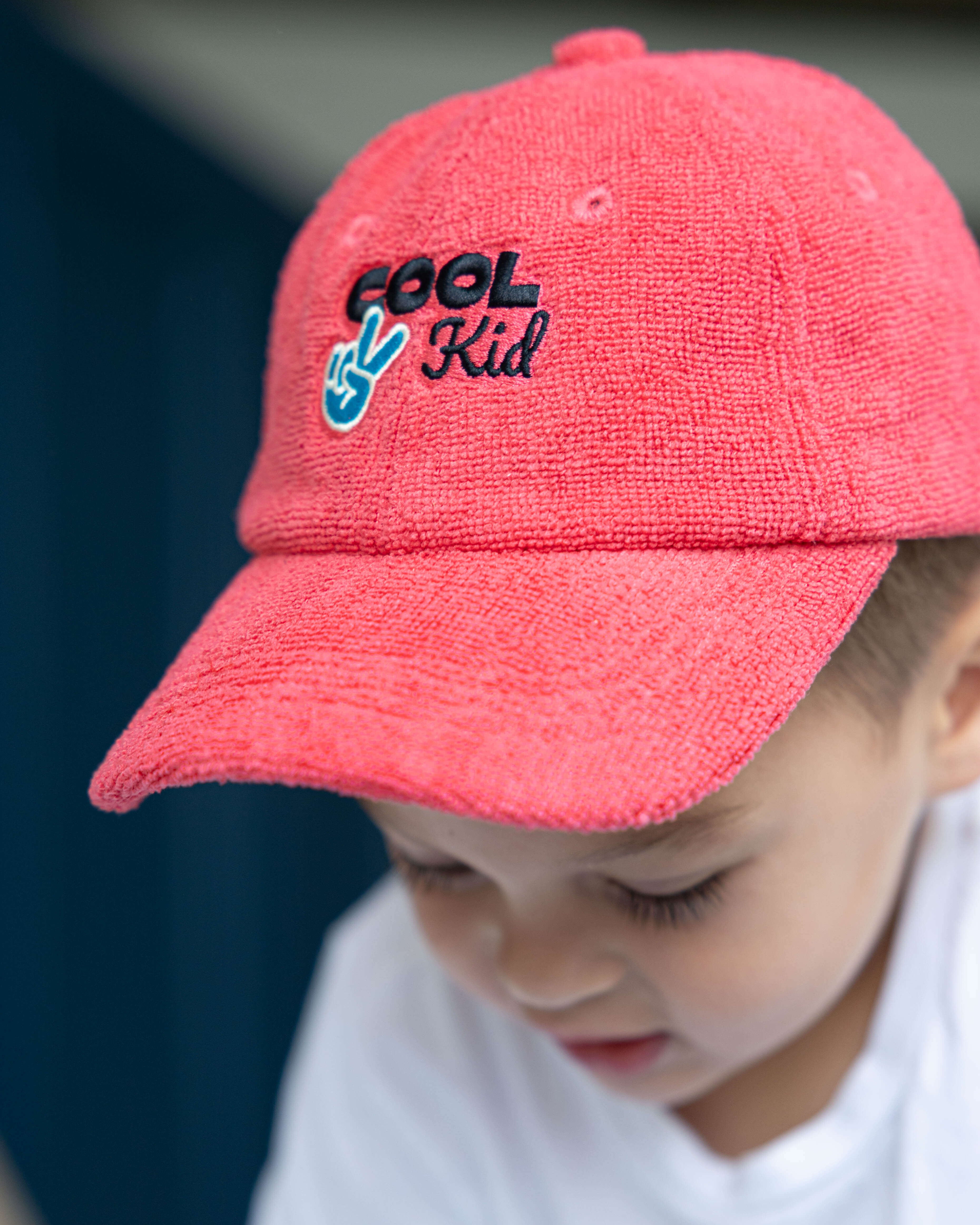 Child wearing a red cap with 'Cool Kid' text and peace sign.
