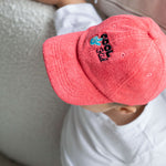 Child wearing a red cap with a cool kid logo, sitting on a couch.