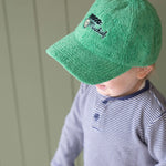 Child wearing a green cap with a logo against a light green wall.