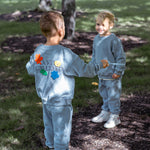 Two children in matching outfits standing outdoors on a grassy area.