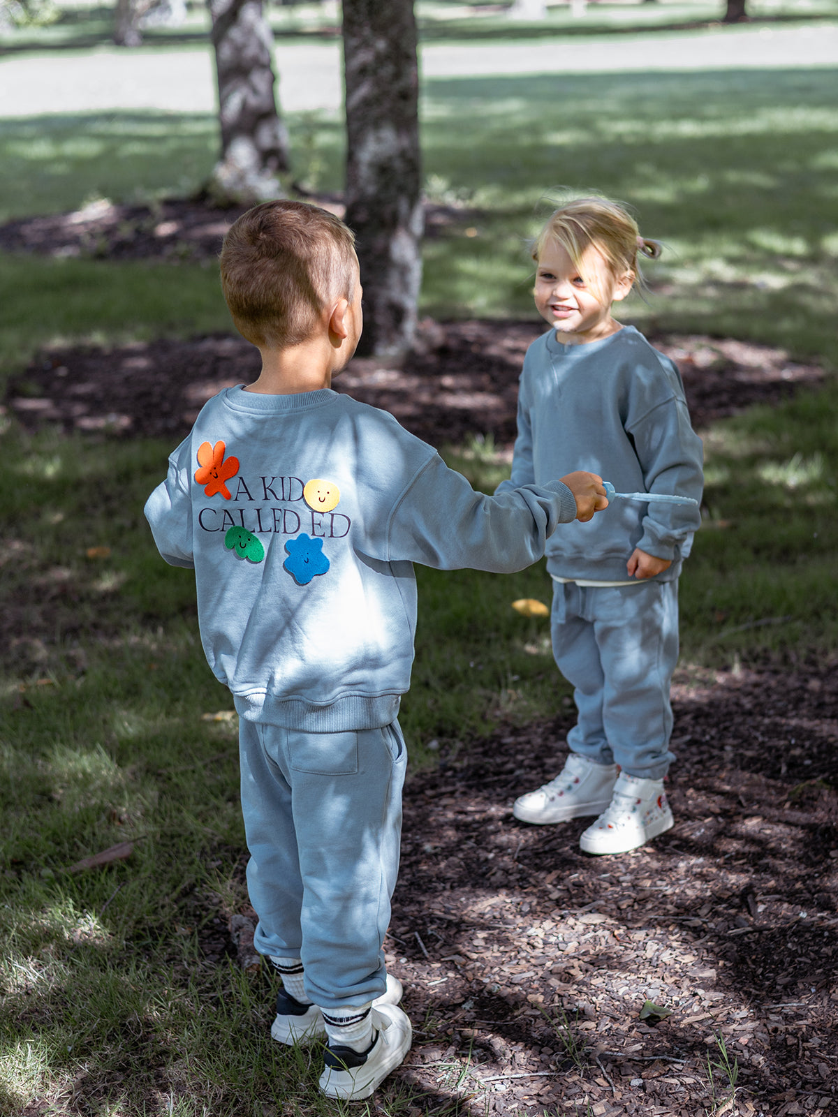 Two children in matching outfits standing outdoors on a grassy area.