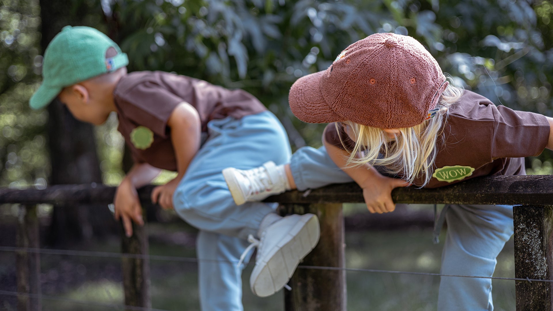 Two children playing on a wooden fence outdoors with trees in the background