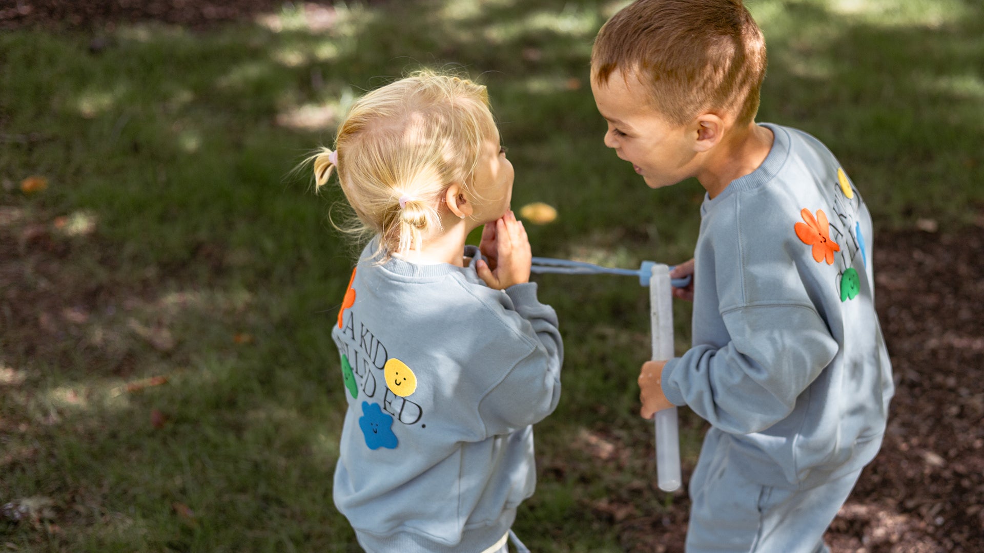 Two children in matching outfits playing outdoors with a toy.