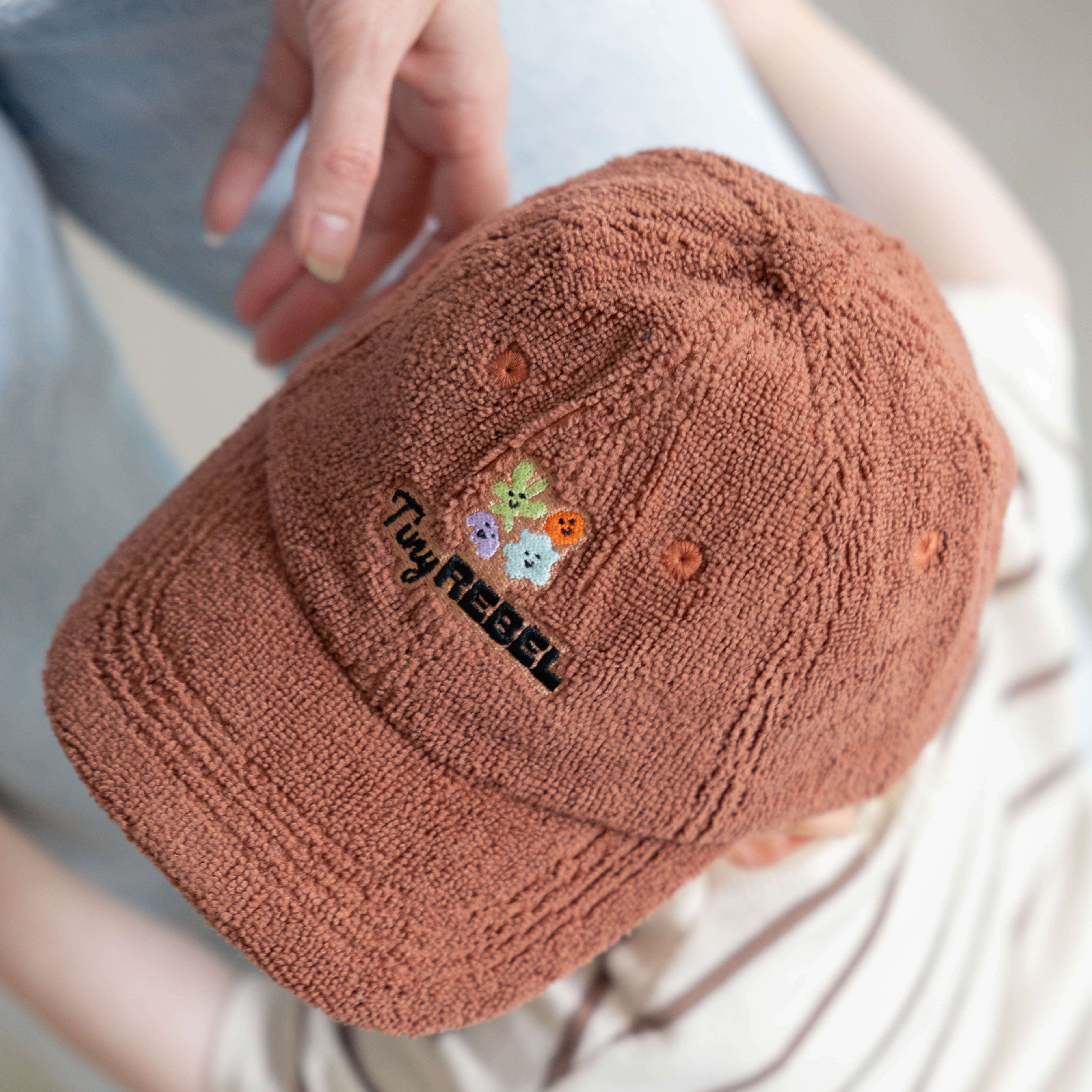 Brown textured cap with colorful embroidery worn by a toddler