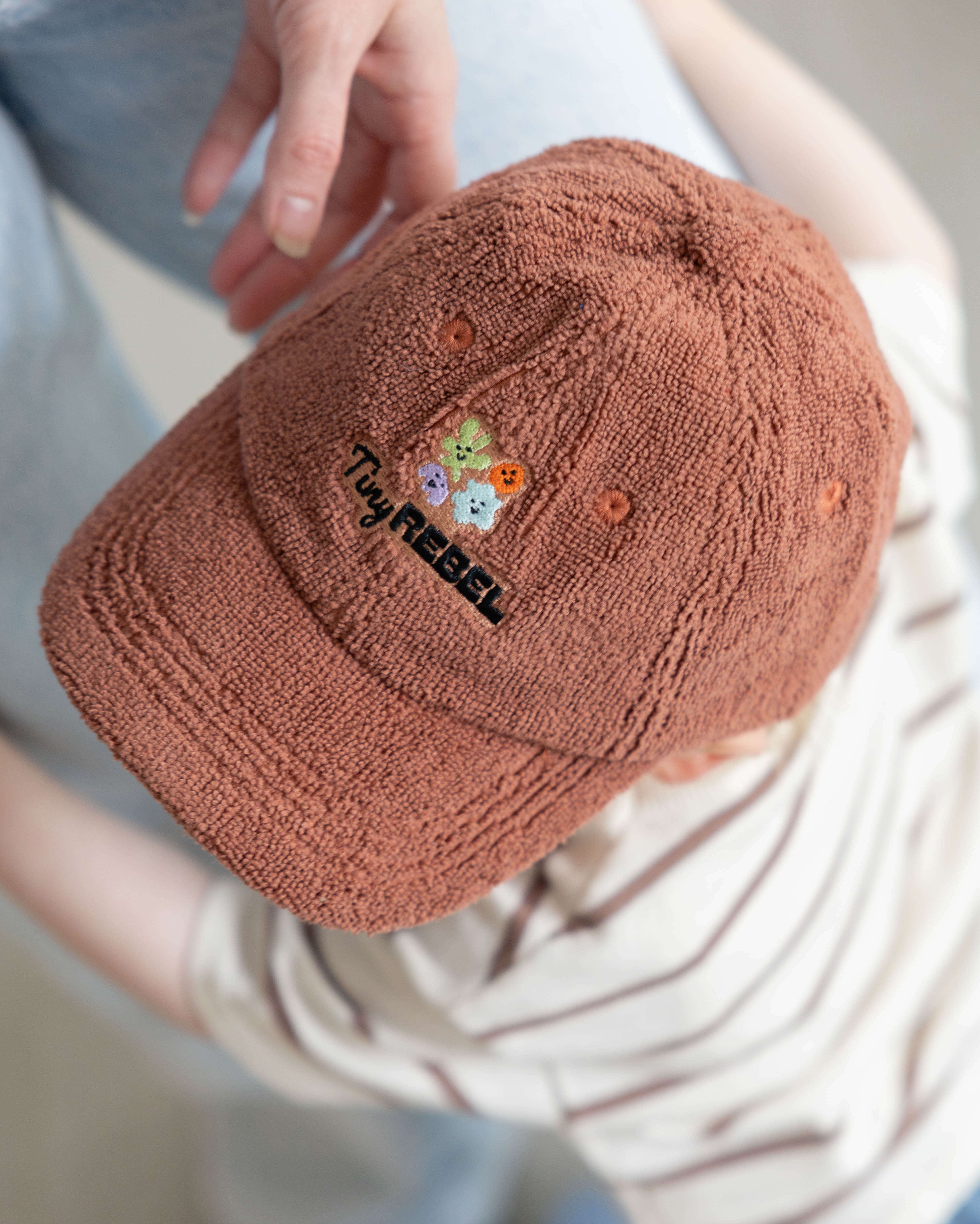 Brown textured cap with colorful embroidery worn by a toddler