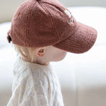 Child wearing a brown cap sitting on a white couch