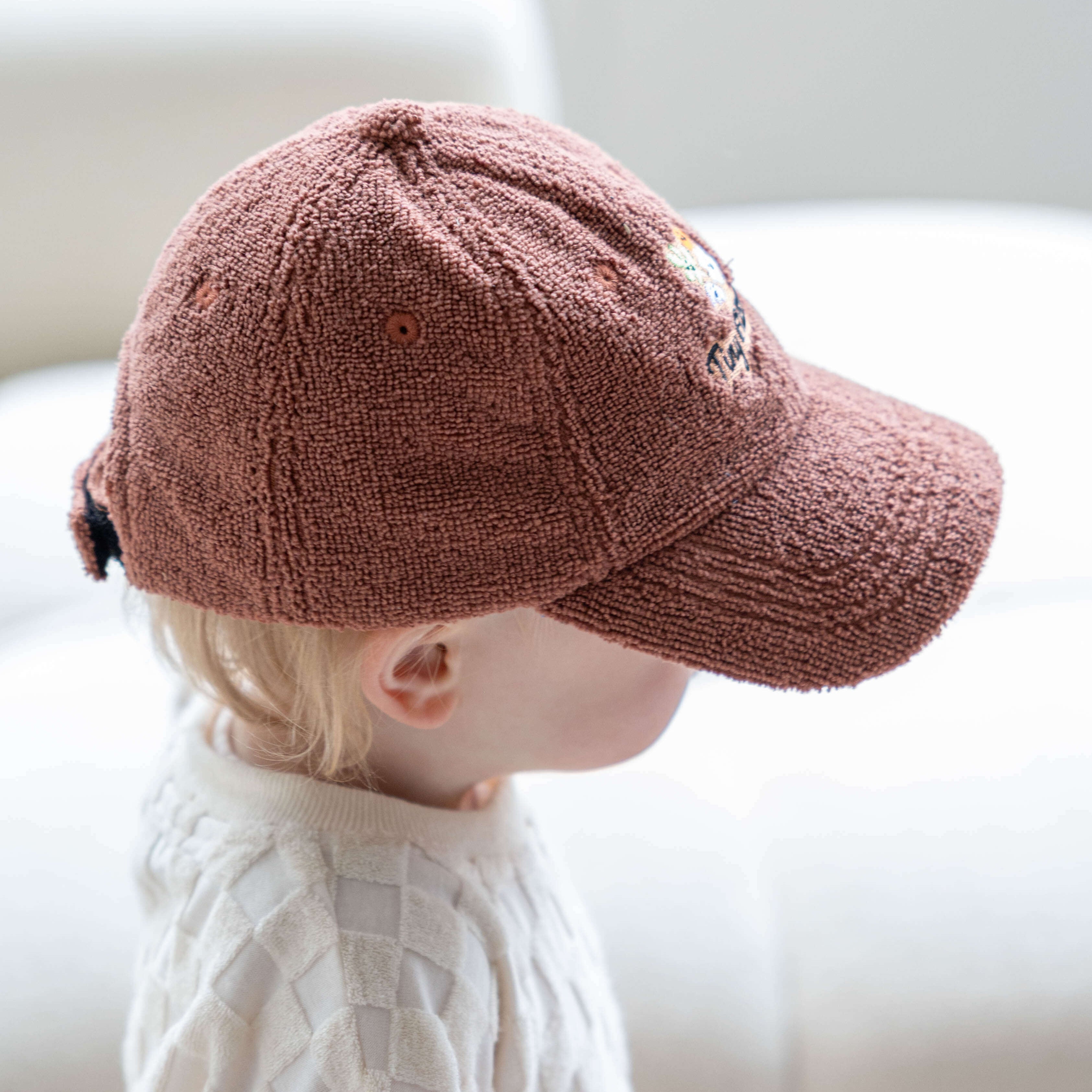 Child wearing a brown cap sitting on a white couch