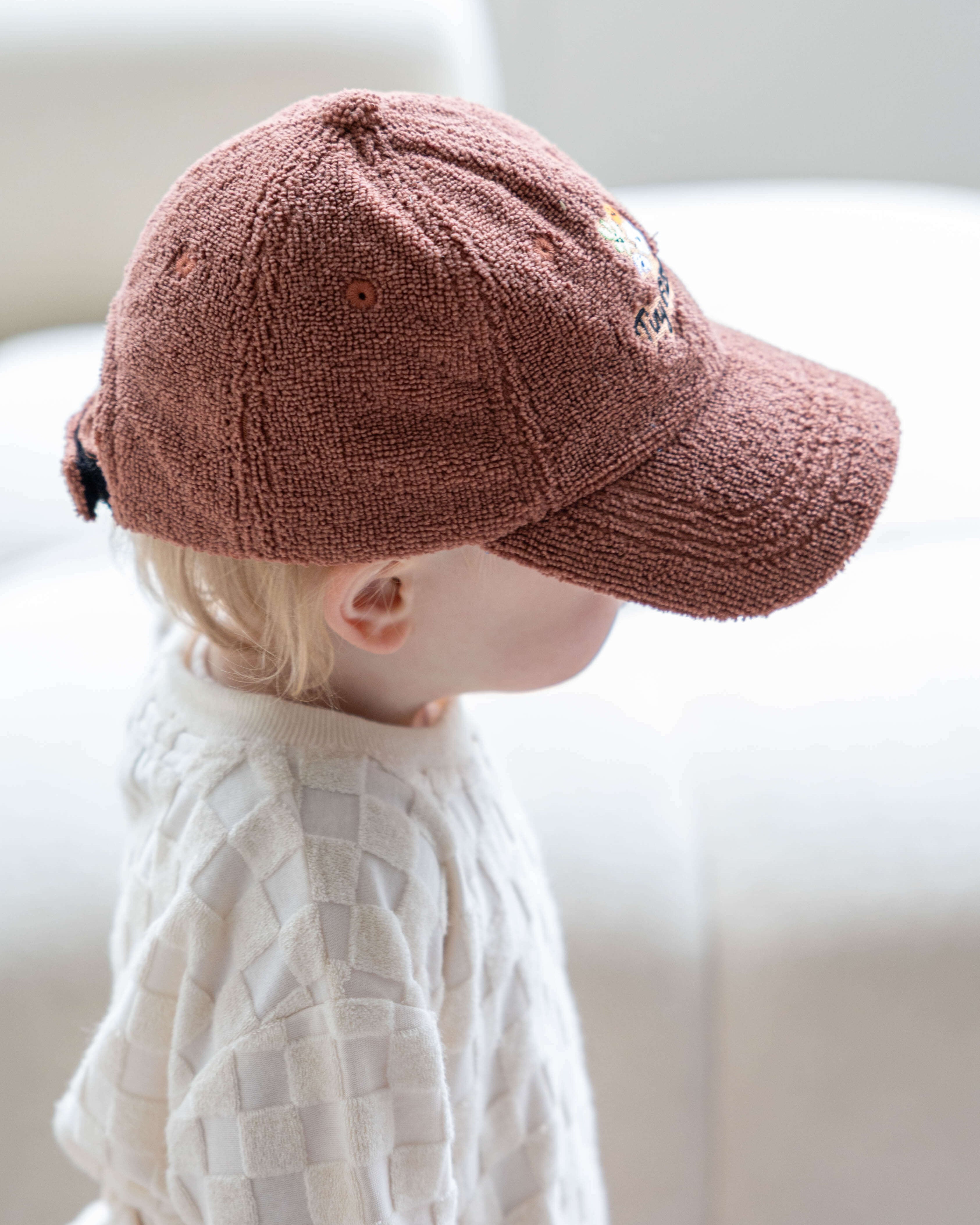 Child wearing a brown cap sitting on a white couch