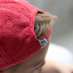 Close-up of a child wearing a red cap with a brand logo on a blurred background