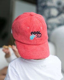 Person wearing a red cap with 'Cool Kid' text, sitting on a couch.
