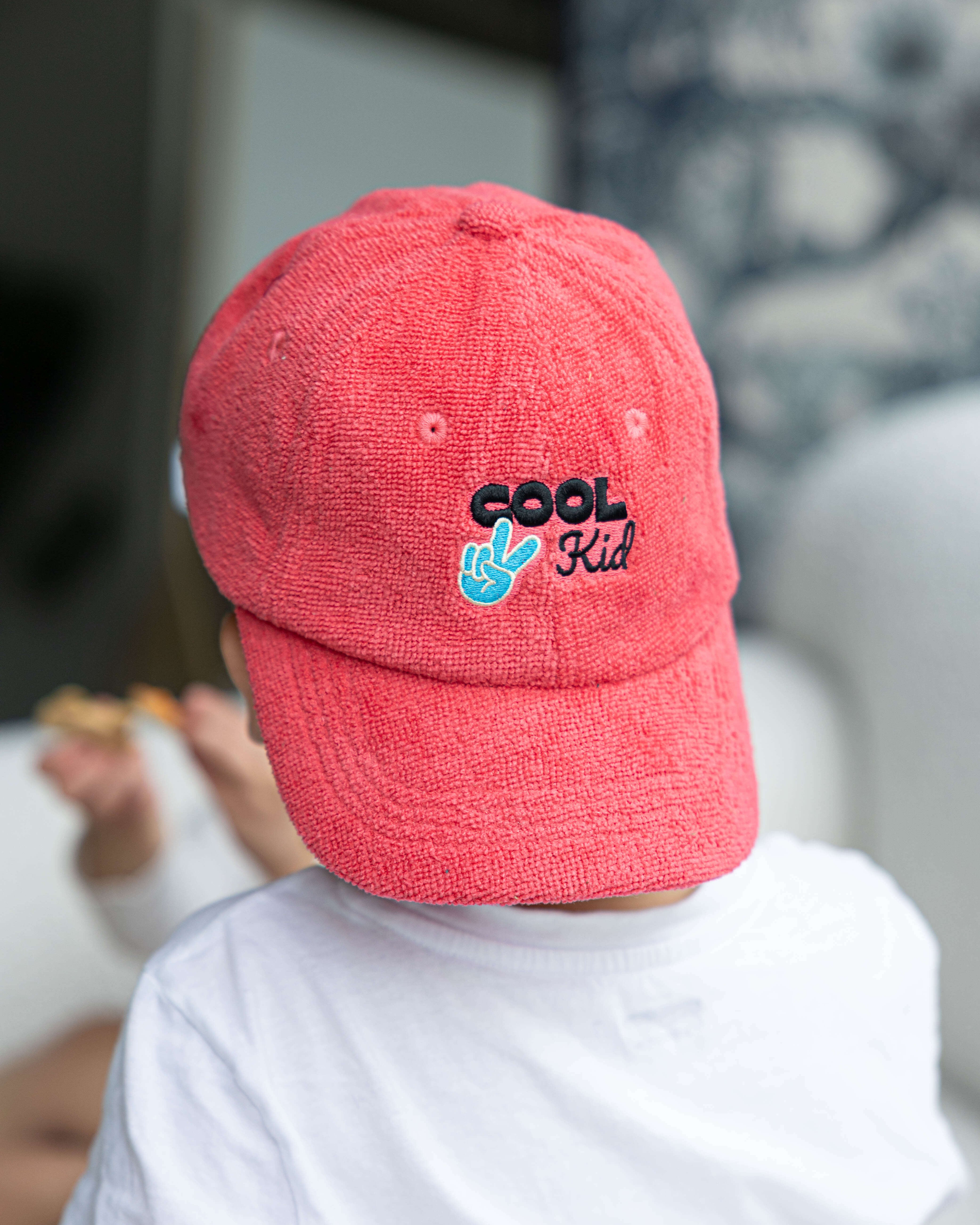 Person wearing a red cap with 'Cool Kid' text, sitting on a couch.