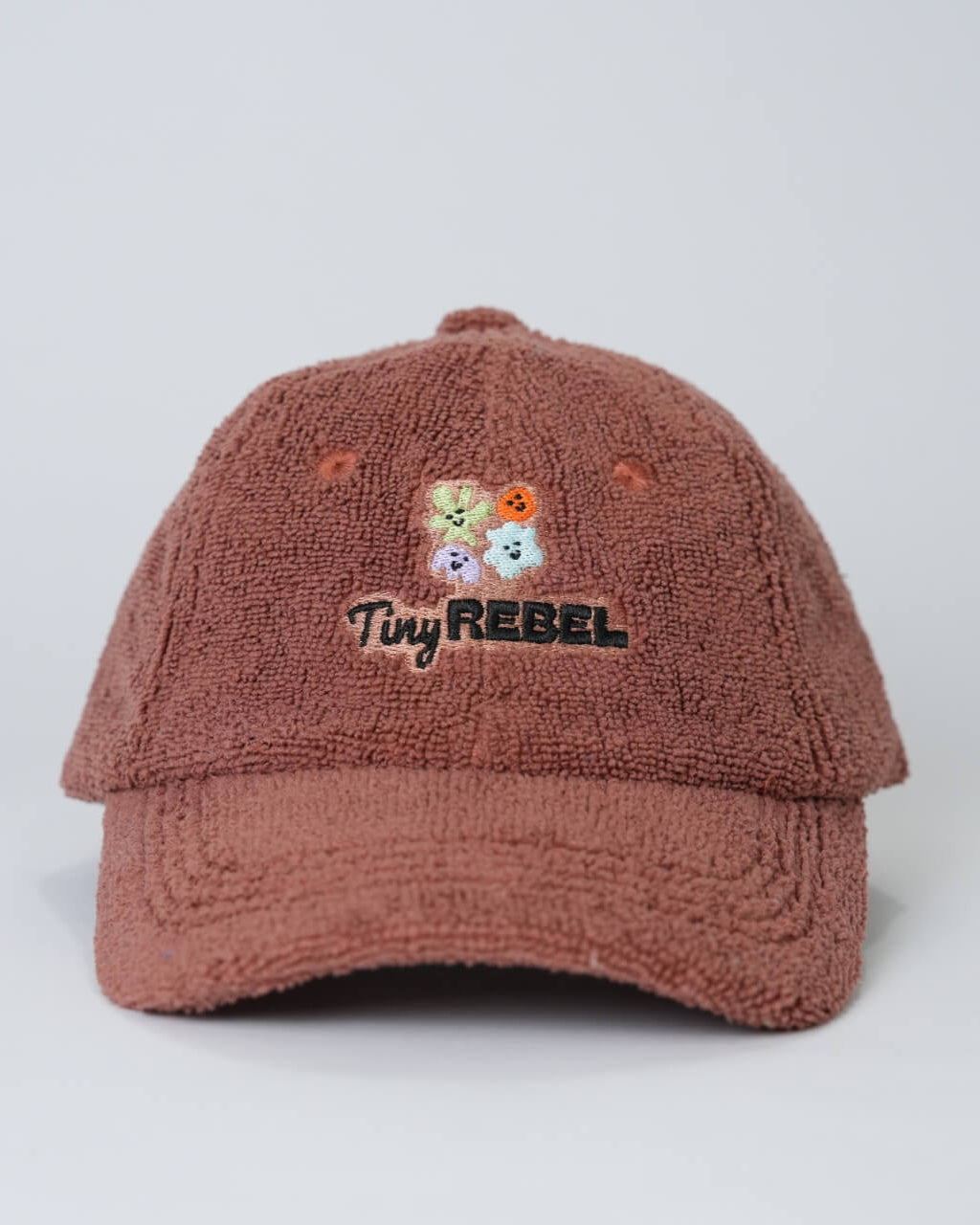 Brown textured cap with 'Tiny Rebel' logo and floral design on a light gray background