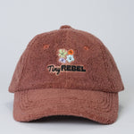 Brown textured cap with 'Tiny Rebel' logo and floral design on a light gray background