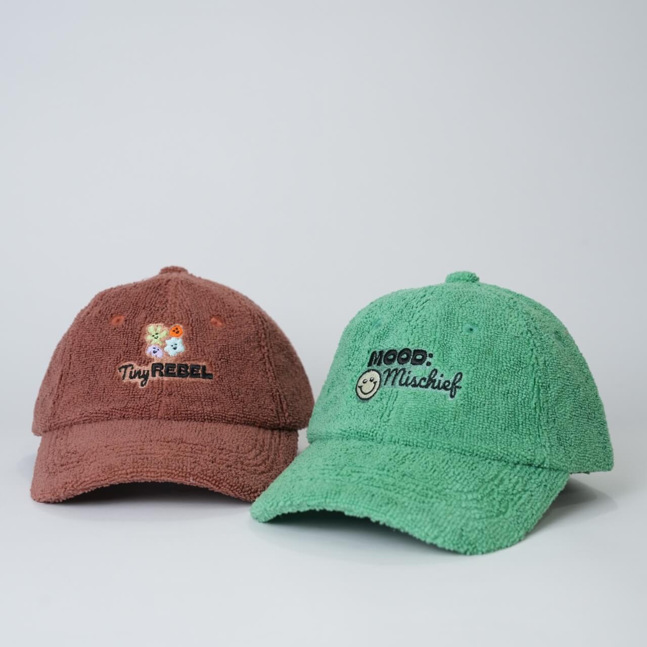 Two textured baseball caps, one brown and one green, on a light gray background.