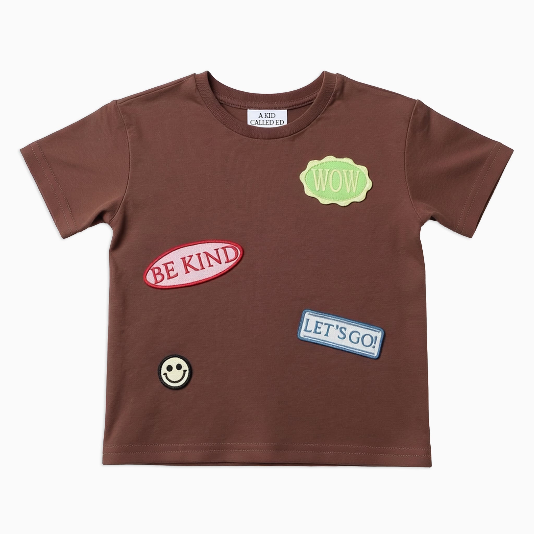 Brown t-shirt with various patches including 'Be Kind', 'Let's Go!', and a smiley face on a white background.