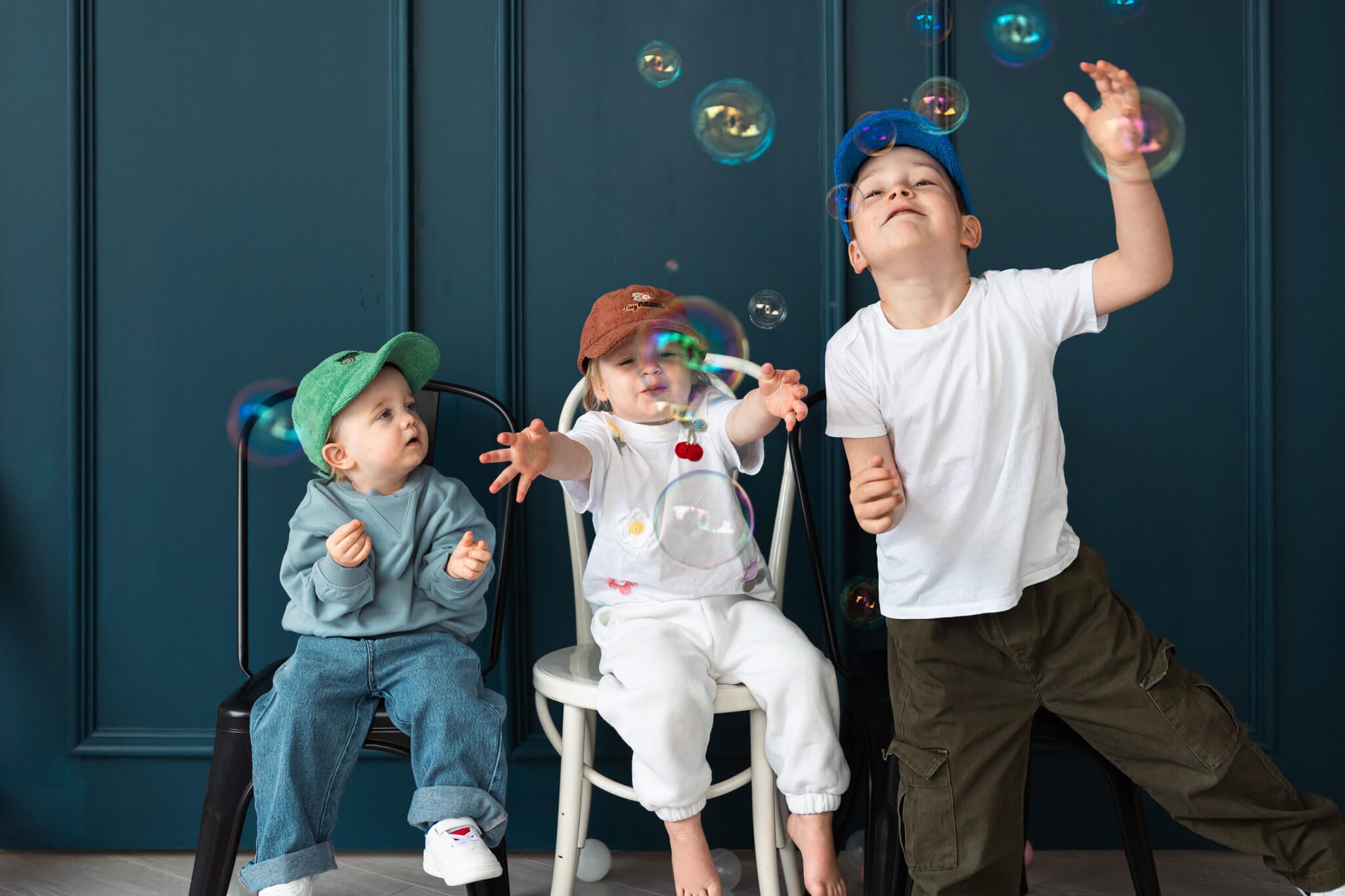Three children playing with bubbles against a dark blue wall.