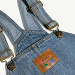 Close-up of the adjustable strap and leather logo patch on the kids denim overalls