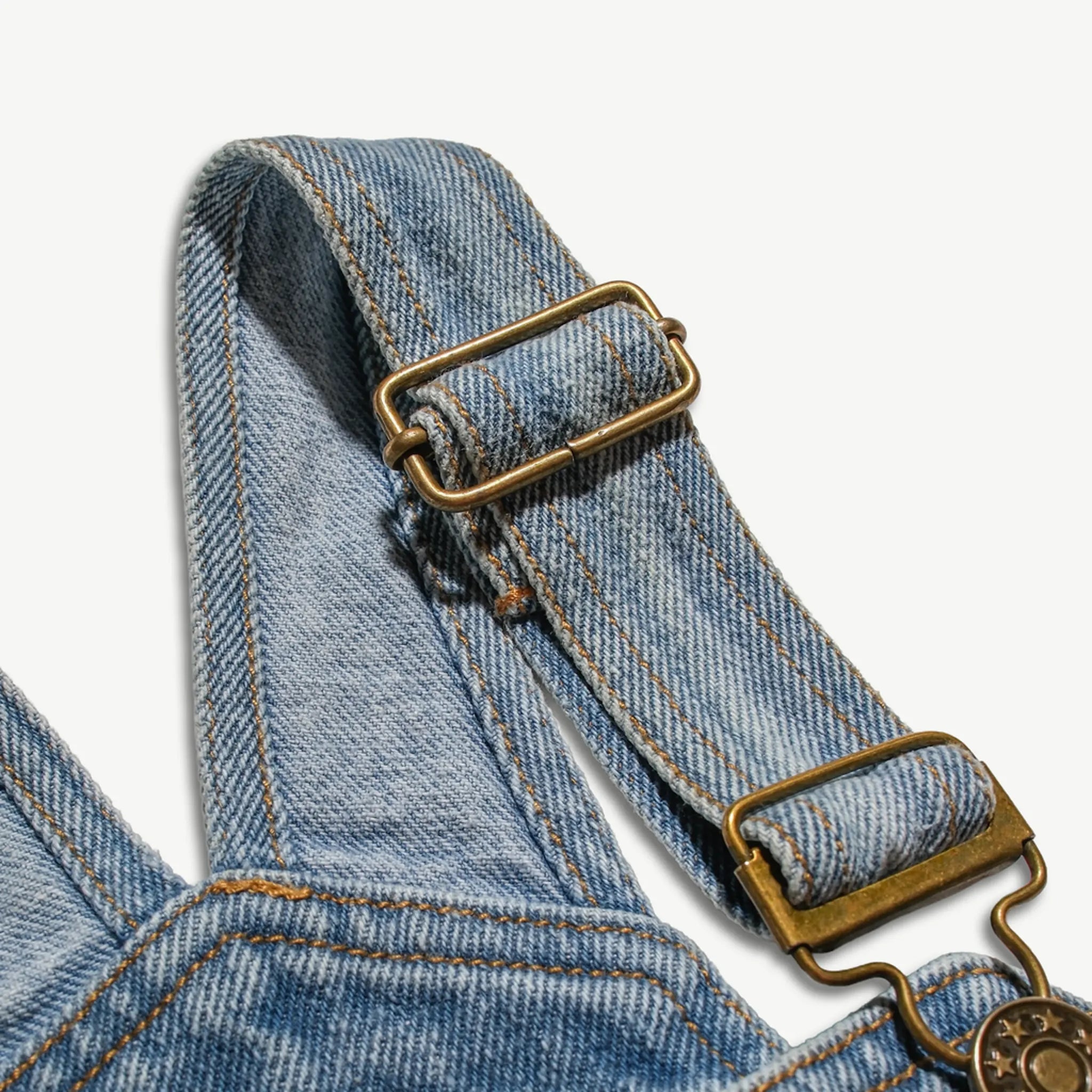 Close-up of the adjustable brass buckle on the kids denim overalls