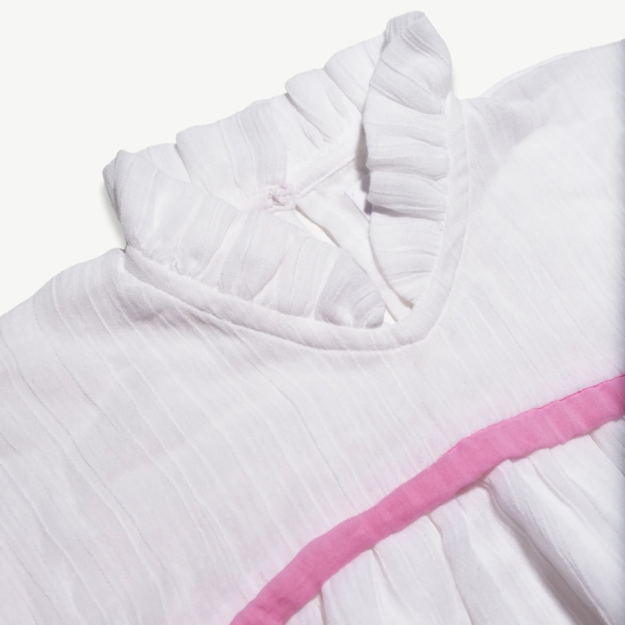 Close-up of the neckline frill and pink trim on the organic cotton muslin dress