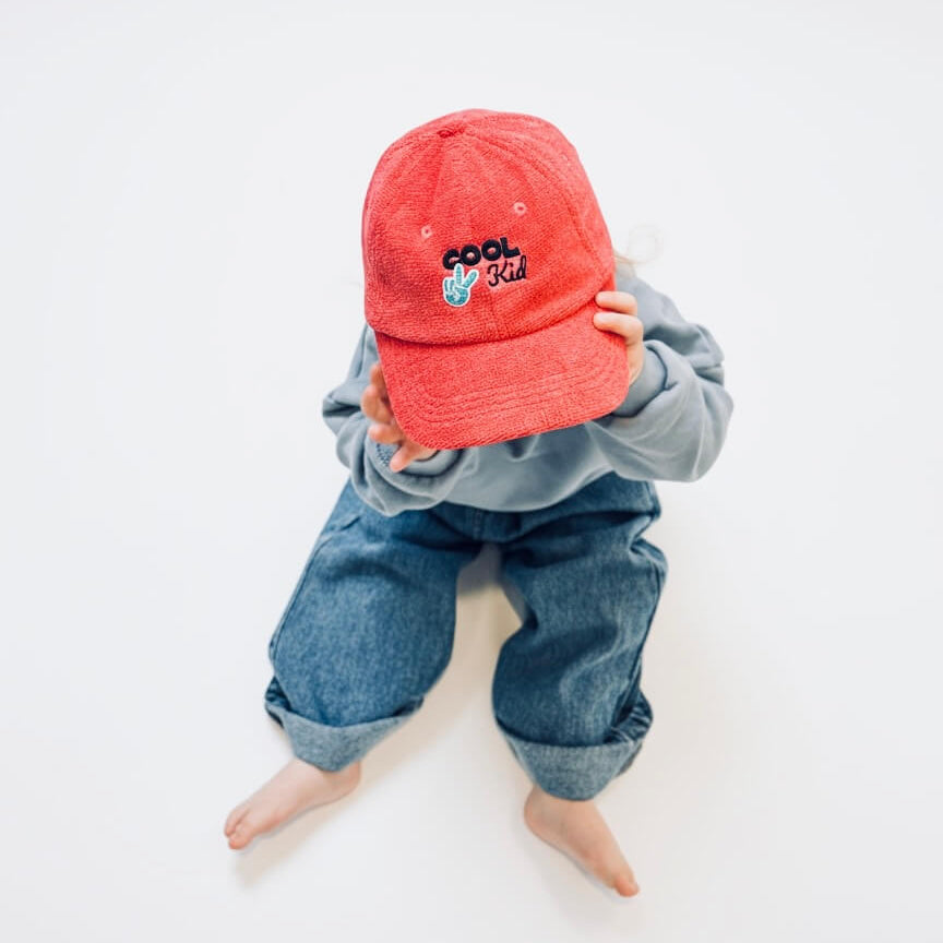 Child wearing a red cap with text and blue pants on a white background