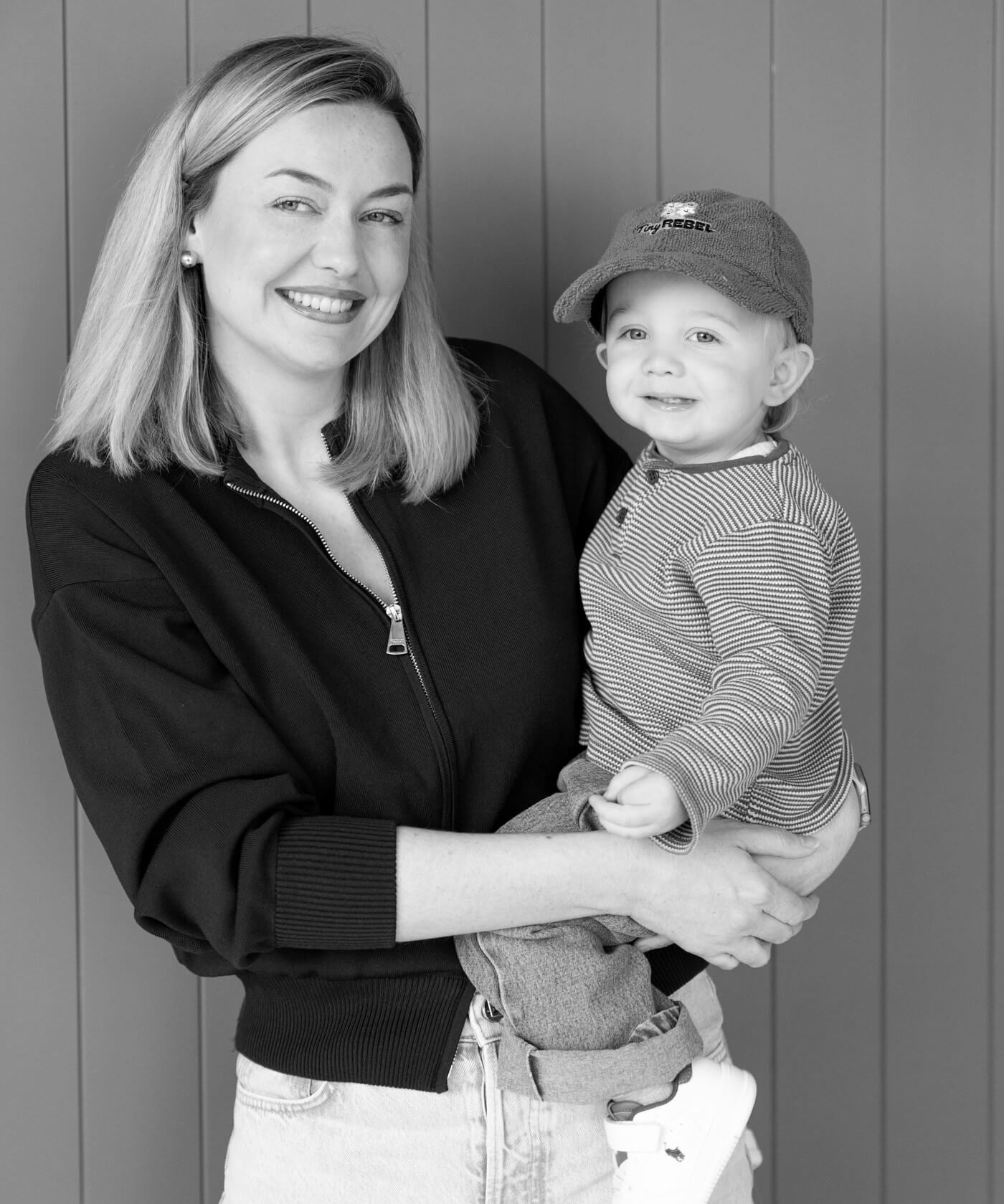 Black and white photo of a woman holding a child in a cap against a wooden background