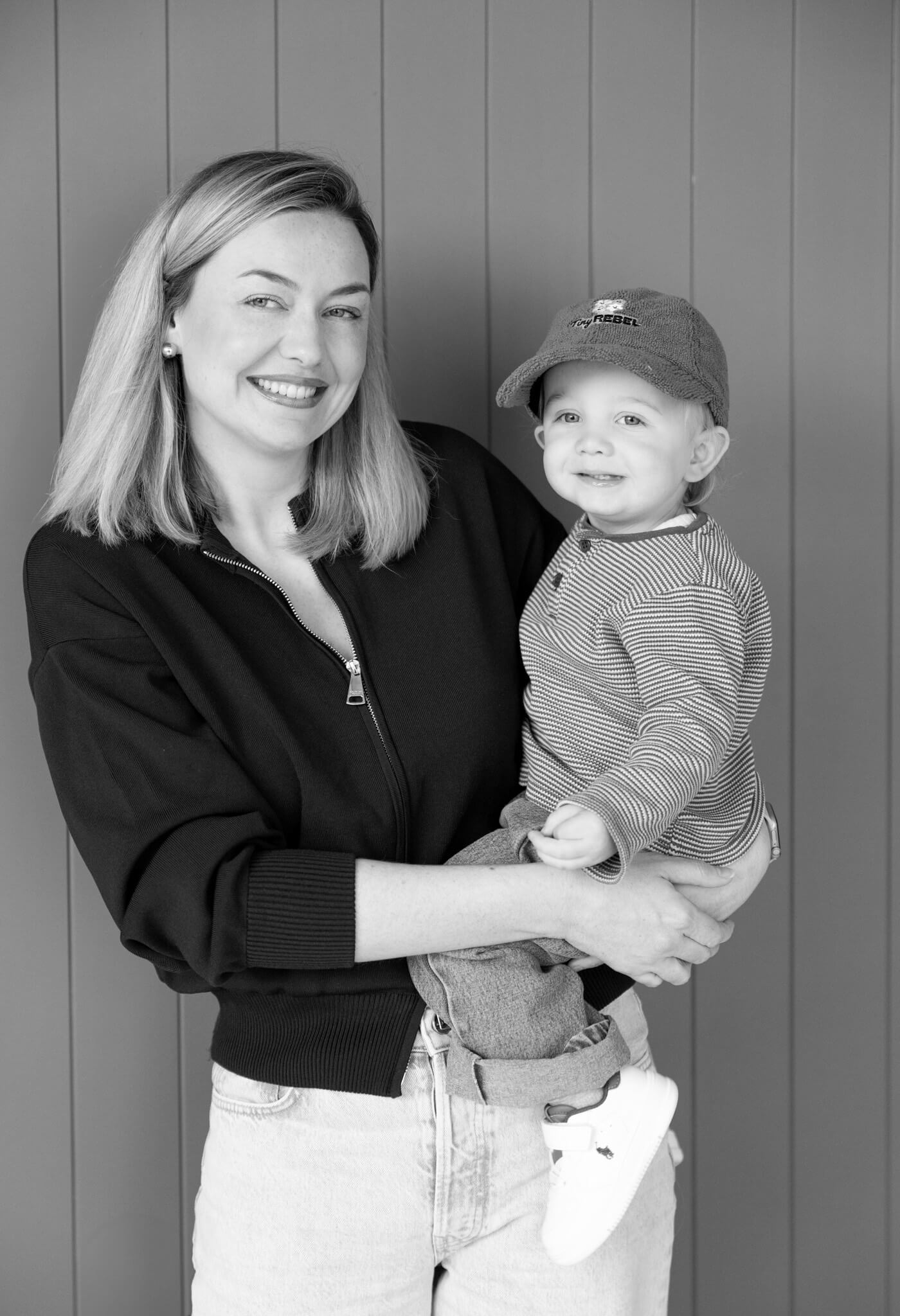 Black and white photo of a woman holding a child in a cap against a wooden background